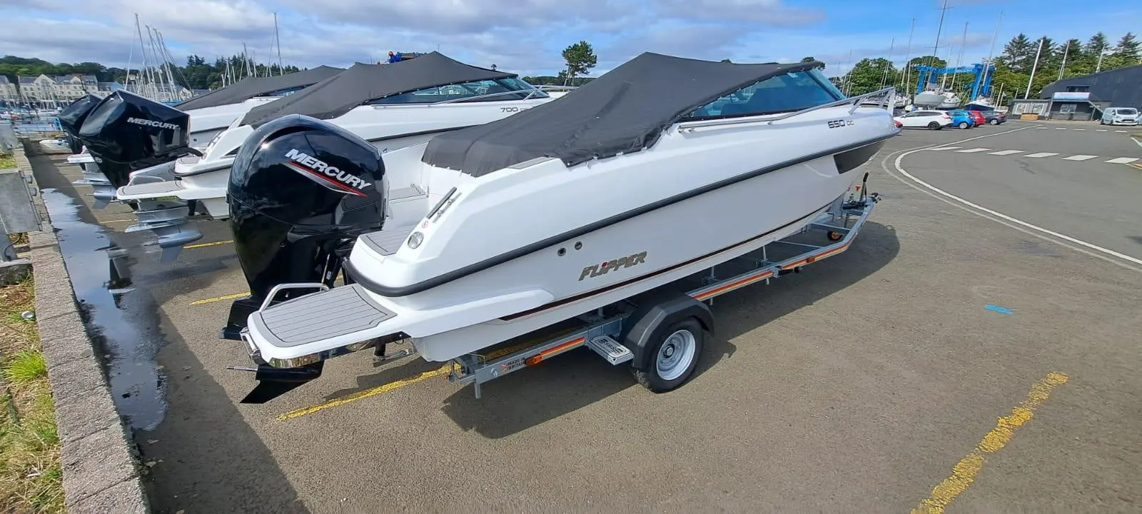 Side view of a white Flipper boat with a Mercury outboard motor, moored at a marina alongside other boats.